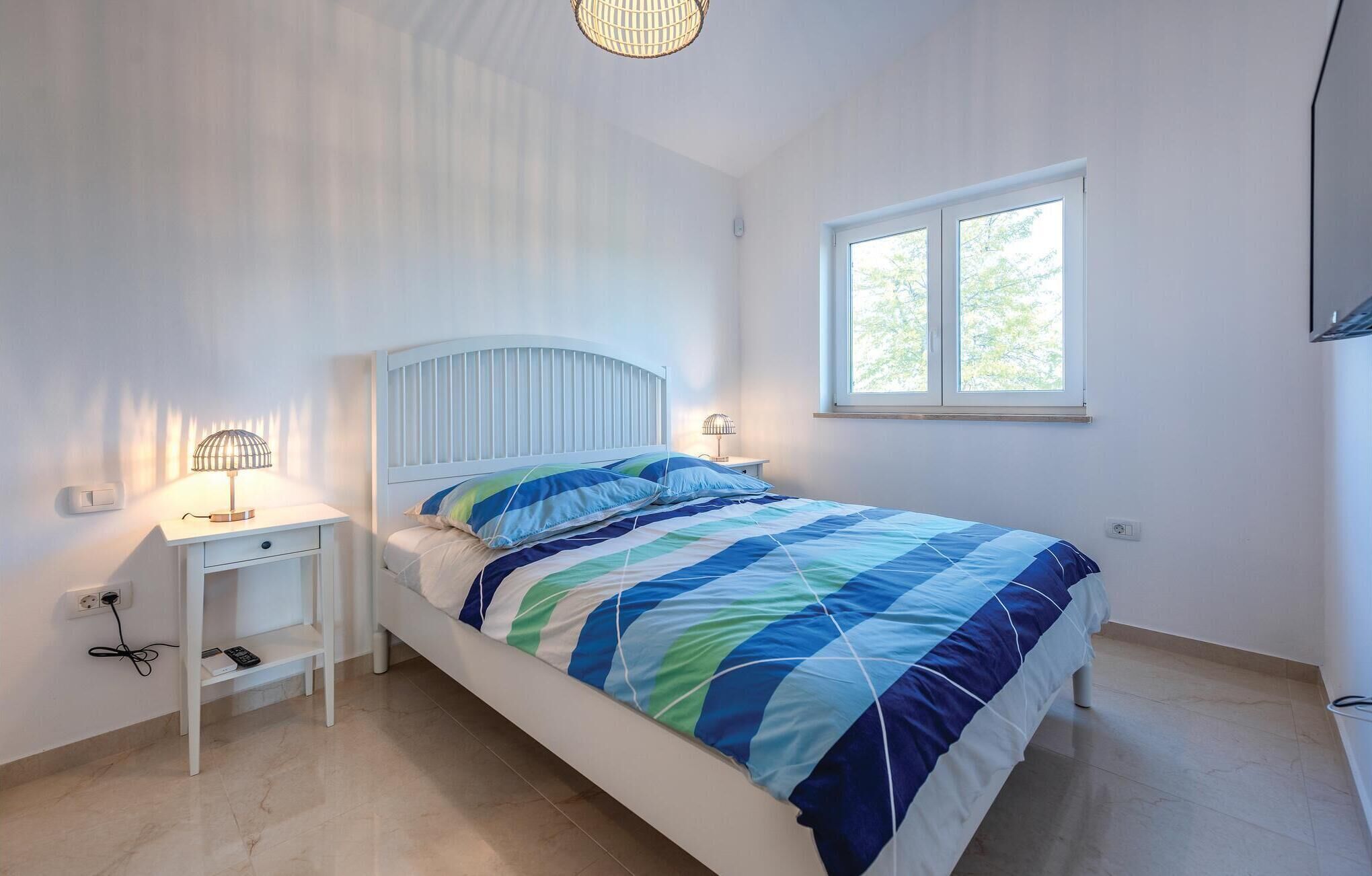 Un dormitorio con cama, dos mesitas de noche, una ventana y una lámpara en el techo.
