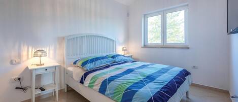 Un dormitorio con cama, dos mesitas de noche, una ventana y una lámpara en el techo.