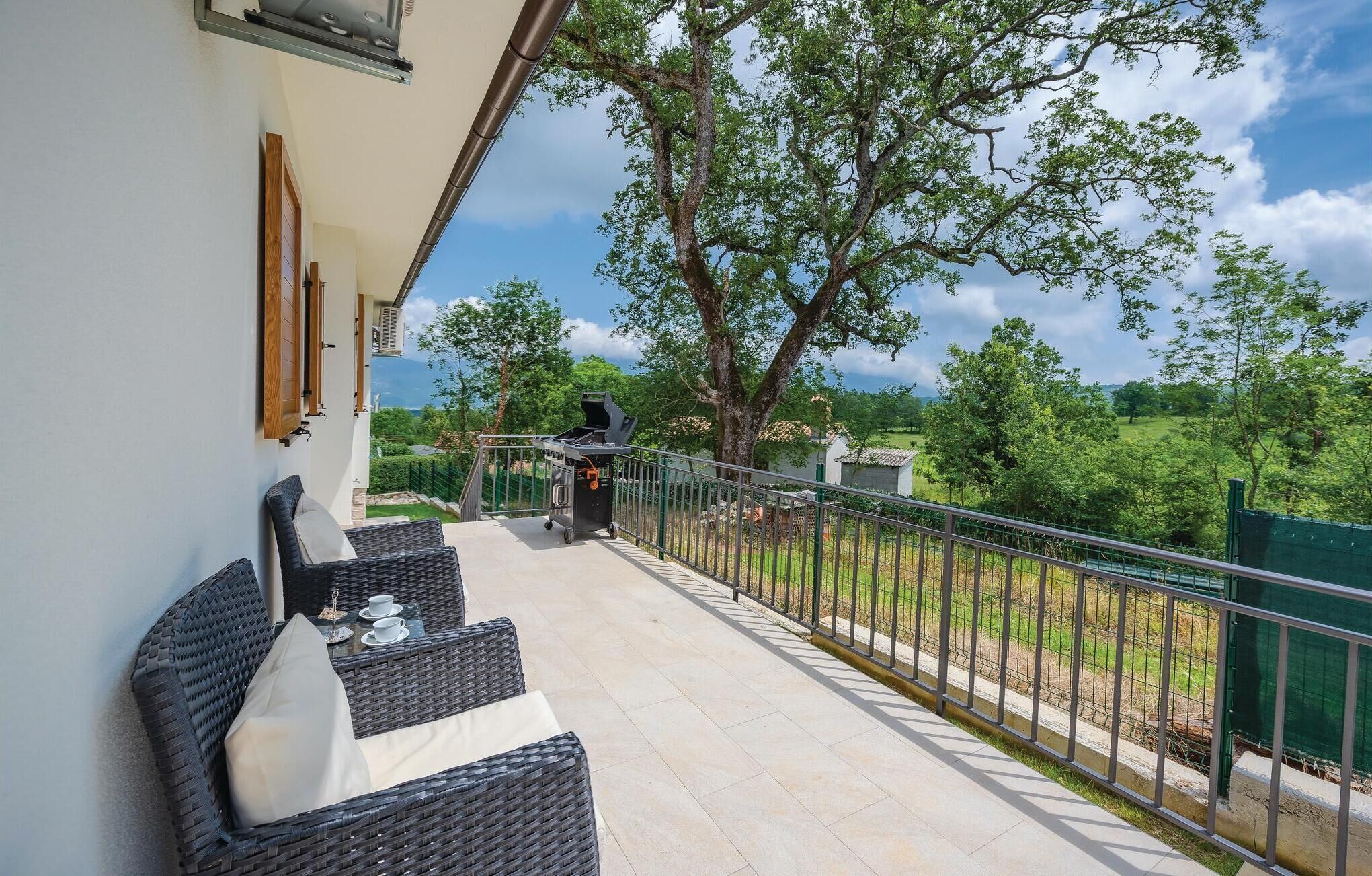 A balcony with wicker furniture and a grill, overlooking a green landscape.
