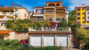 Un immeuble résidentiel à plusieurs étages, doté de balcons, d’un garage et d’un mur en pierre.