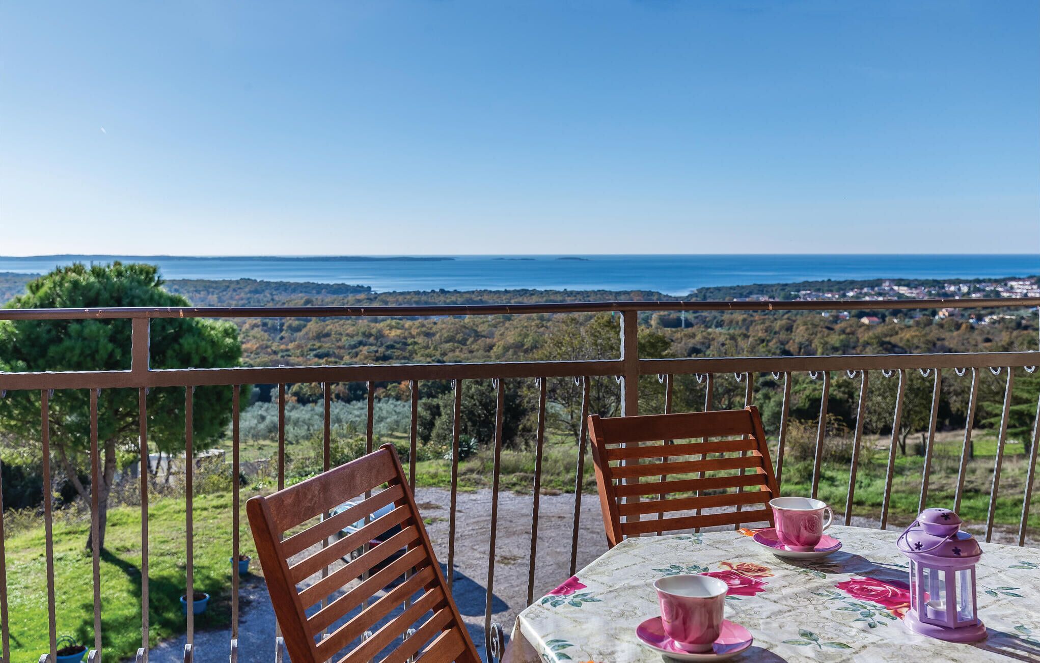 Un balcón con una mesa lista para dos personas, con vistas a un paisaje marino y tierras lejanas.