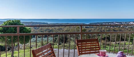 Un balcon avec une table dressée pour deux personnes, offrant une vue panoramique sur la mer et le paysage environnant.
