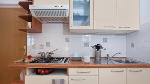 A kitchen with a gas stove, sink, and cabinets. There is a fruit bowl with apples, a kettle, and a coffee maker on the counter. - Awesome apartment in Rabac with WiFi (Rabac)