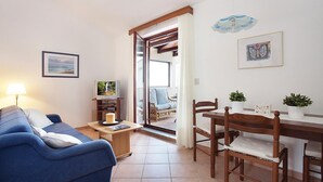 A cozy living room with a blue sofa, a wooden dining table with chairs, a TV on a wooden stand, and a view of the outdoors through a glass door. - Awesome apartment in Rabac with WiFi (Rabac)