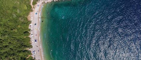 Vista aèria d'una platja amb aigües turqueses cristal·lines, sorra daurada i una zona boscosa densa.