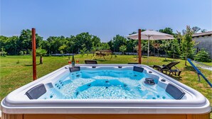 Un bain à remous dans un jardin, avec une pelouse verdoyante, un hamac et une structure en bois.