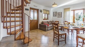 Un vaste espace de vie agrémenté d’un escalier en colimaçon en bois, d’une table à manger pour quatre personnes, d’un canapé et d’une grande fenêtre avec des stores.