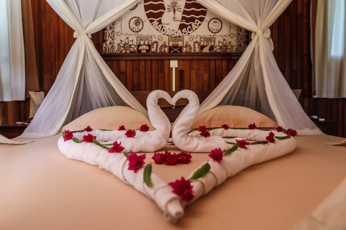 A bed with a canopy, decorated with towels shaped like swans and red flowers.