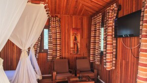 Una habitación acogedora con paredes de madera, una cama con dosel, dos sillones, una mesita y un televisor montado en la pared.