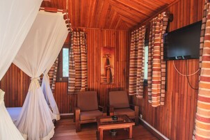 Una habitación acogedora con paredes de madera, una cama con dosel, dos sillones, una mesita y un televisor montado en la pared.