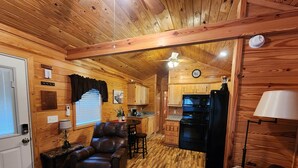 A cozy cabin interior with a wooden floor, leather seating, a kitchen area, and a ceiling fan.