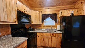 A compact kitchen with wooden cabinets, a black refrigerator, a microwave, a stove, and a sink.