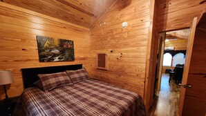 A wooden-paneled bedroom with a bed, a nightstand, a lamp, and a painting of a landscape.