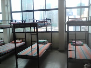 Camas literas con ropa de cama a rayas en una habitación con ventanas amplias y vistas a edificios.