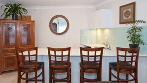 A dining area with four wooden chairs, a wooden cabinet, a round mirror, and a kitchen counter with a sink. - Waterfront on Manly Harbour (Manly)