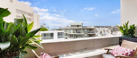 A balcony with two wooden chairs, a potted plant, and a view of buildings in the background.