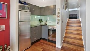 A modern kitchen with grey cabinets, a stainless steel refrigerator, and a wooden staircase. - 713 at the Beach (Manly)