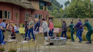 A group of people gathered around a table in an outdoor area with chairs and a thatched-roof building in the background. - Ingagi Park View Lodge (Kinigi)
