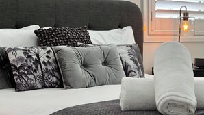 A bed with multiple pillows, a rolled white towel, and a bedside table with a lamp.
