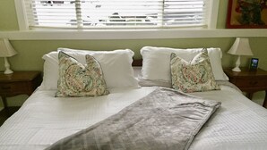 Una cama bien hecha con almohadas estampadas, un plaid gris y una mesita de noche con lámpara.