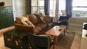 Una sala de estar con un sofá marrón, una mesa de centro de madera, una maleta negra y una silla verde.