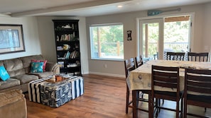 Een woonkamer met een bank, poef, boekenkast, eettafel en stoelen.