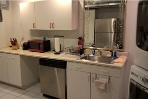 Cozinha compacta com armários brancos, geladeira de aço inoxidável, lava-louças e pia com torneira.
