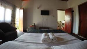 A hotel room with a bed, a chair, a TV mounted on the wall, and a wooden door. - Nature Villa 107 Kandy - Hostel (Kandy)