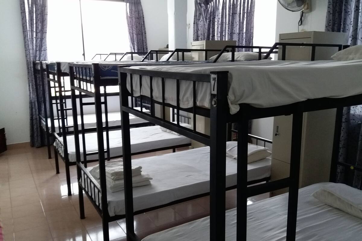 Une chambre de dortoir avec des lits superposés, un ventilateur et des rideaux.