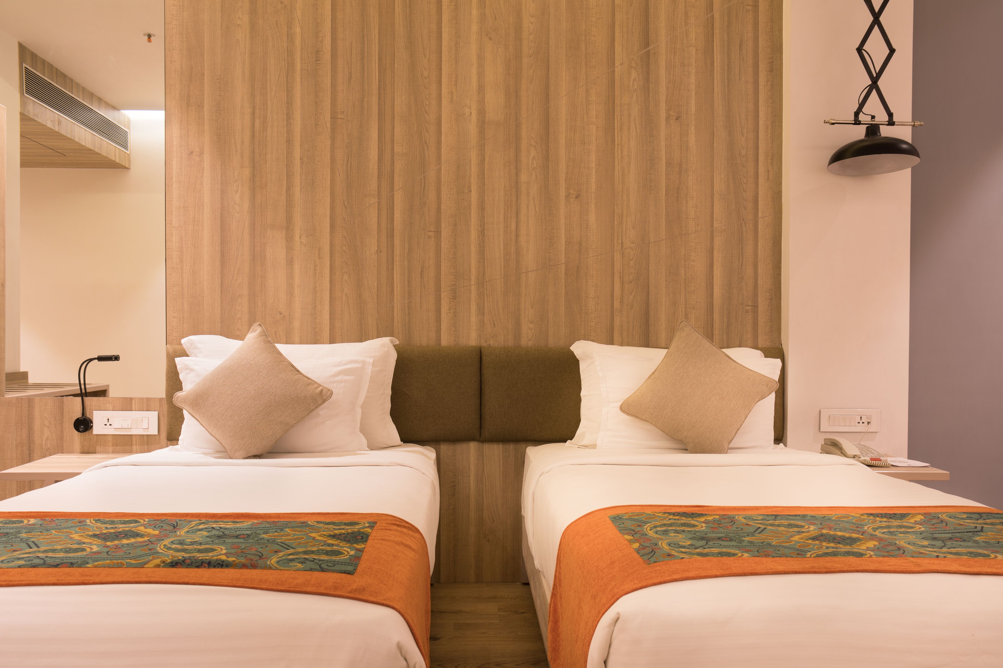 Une chambre d’hôtel avec deux lits, une tête de lit en bois, une table de chevet avec une lampe et un téléphone.