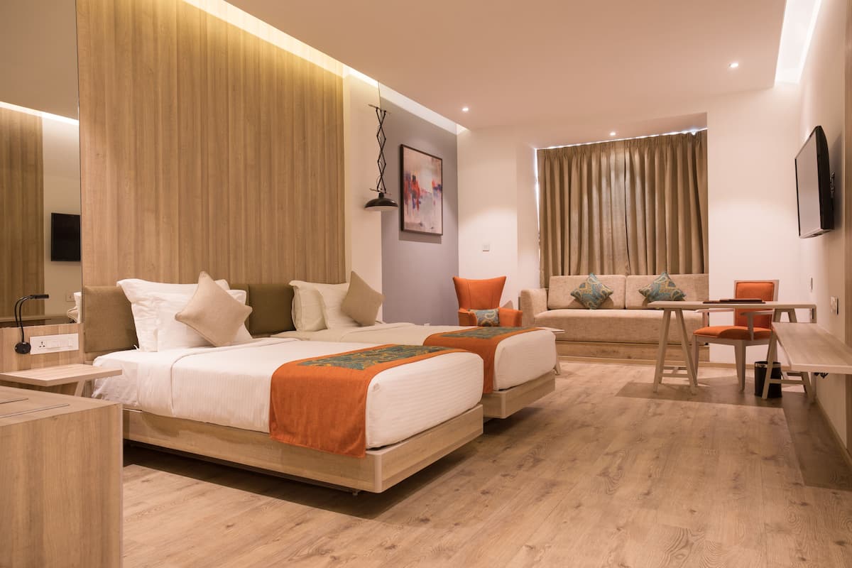 Moderni hotellihuone, jossa on kaksi sänkyä, työpöytä ja sohva.