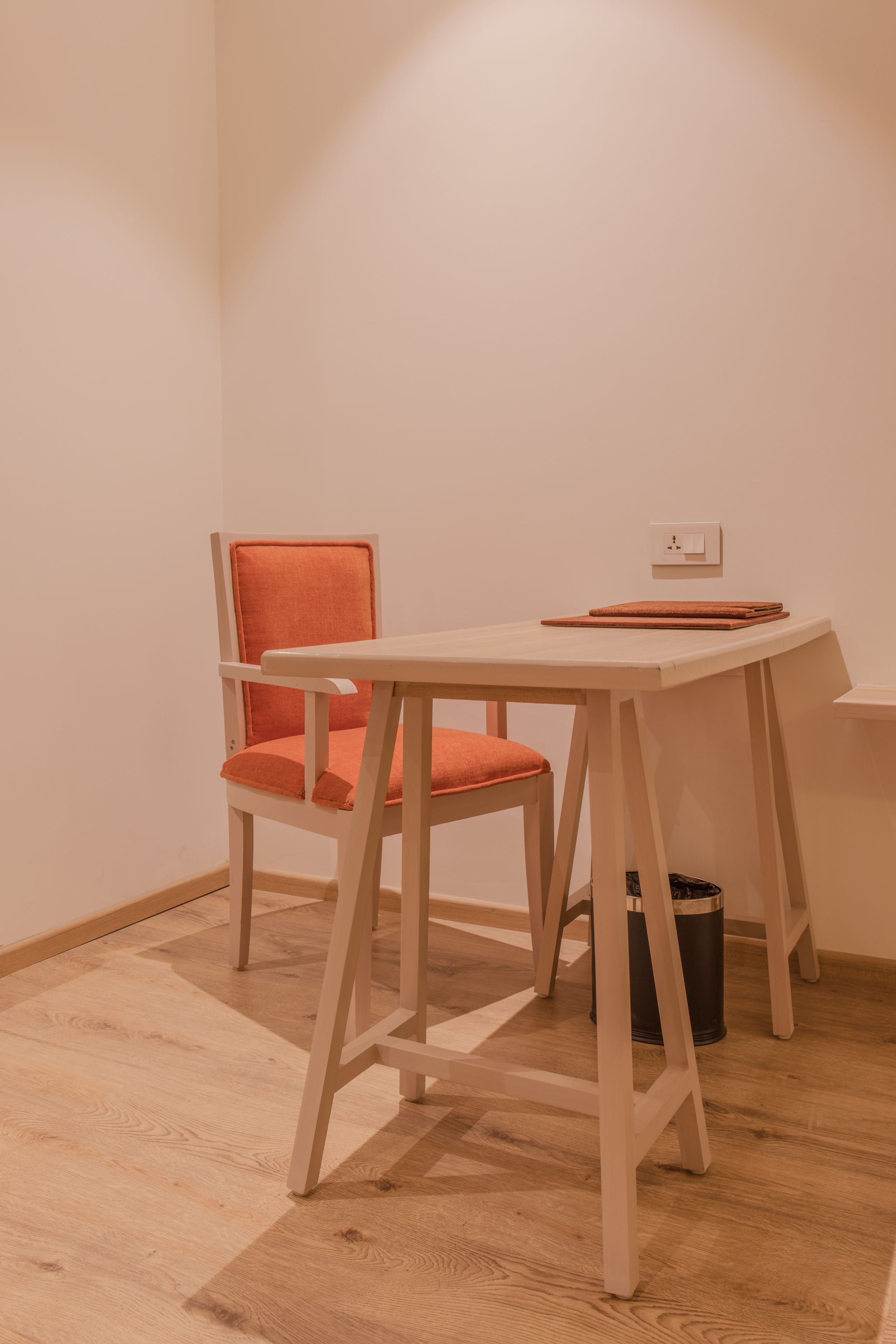 Una habitación pequeña y sencilla con una mesa de madera y una única silla naranja.