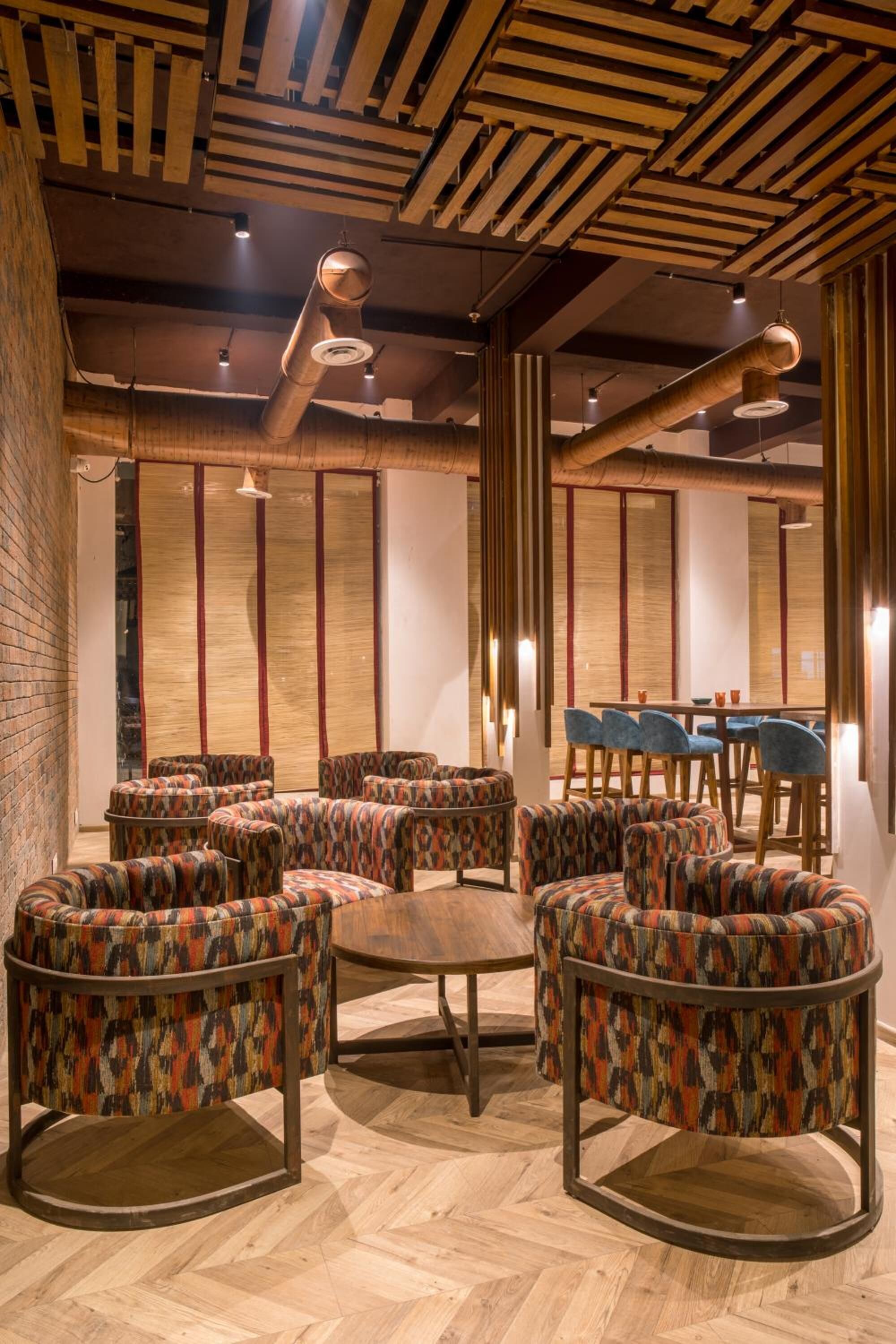 A modern lounge area with patterned armchairs and a wooden table, featuring exposed ceiling beams and a herringbone floor pattern.
