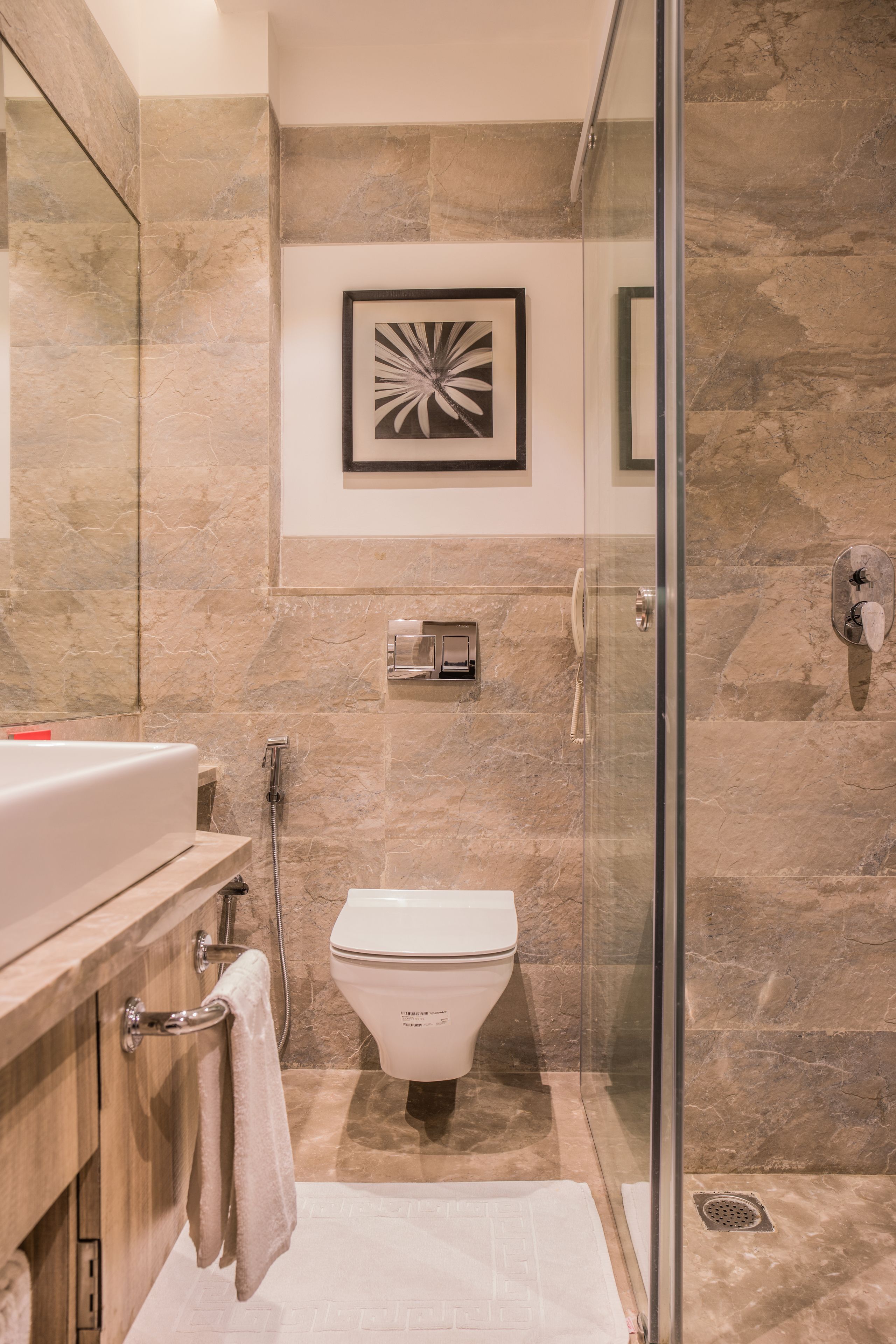 A modern bathroom with a glass shower enclosure, a marble-tiled wall, a white toilet, and a framed abstract artwork above the toilet.