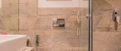 A modern bathroom with a glass shower enclosure, a marble-tiled wall, a white toilet, and a framed abstract artwork above the toilet.