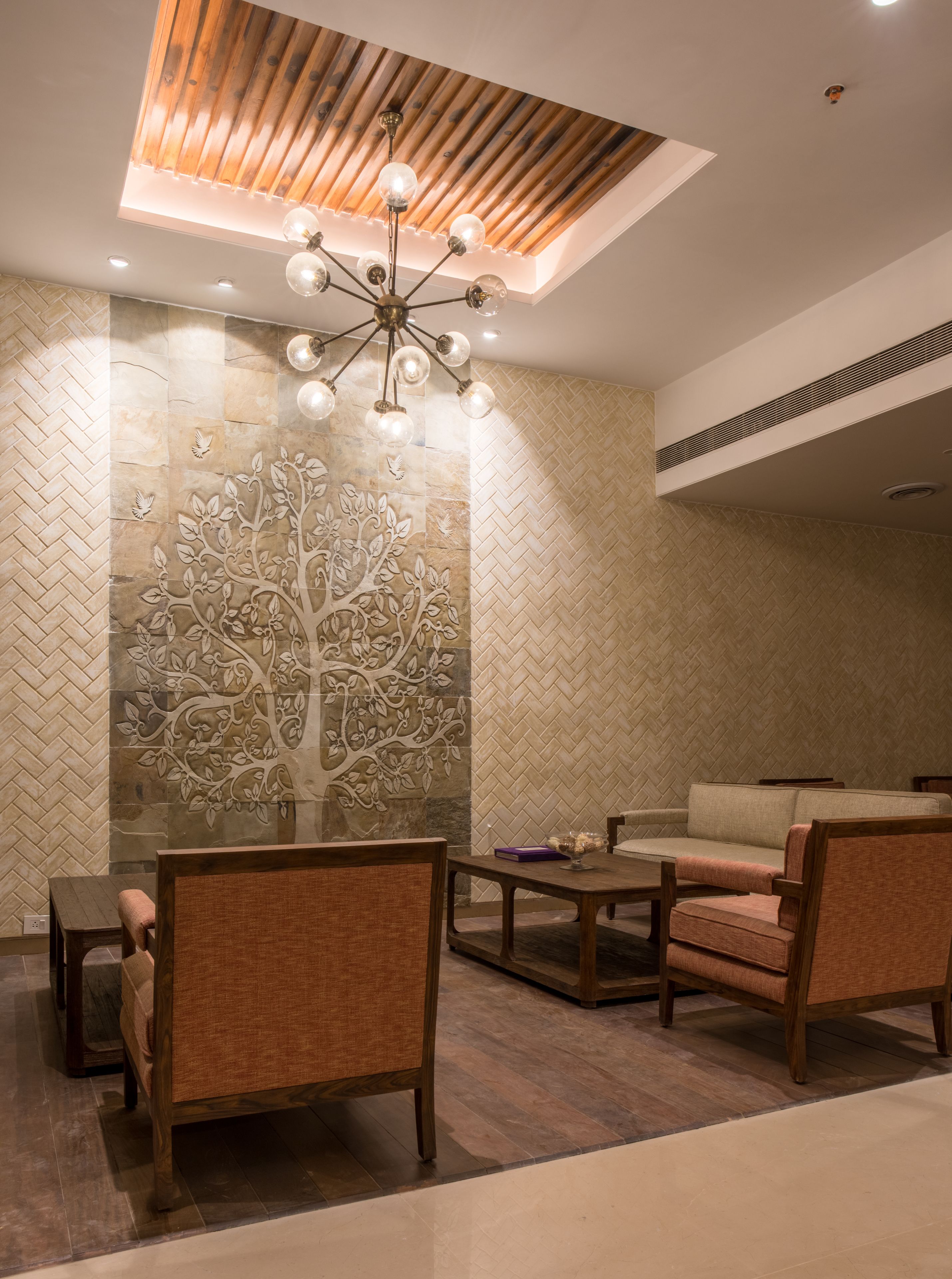 Ein moderner Lounge-Bereich mit Holzboden, einer Wandmalerei mit Baummotiv und einer Sitzecke mit Sofas und Sesseln.