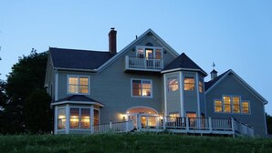 A two-story house with a wrap-around porch, a balcony on the second floor, and a chimney. - High Hill Inn (East Montpelier)