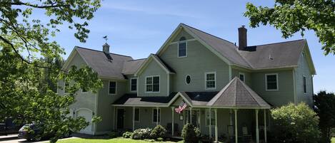 A large, two-story house with a wrap-around porch, a chimney, and a flag.
