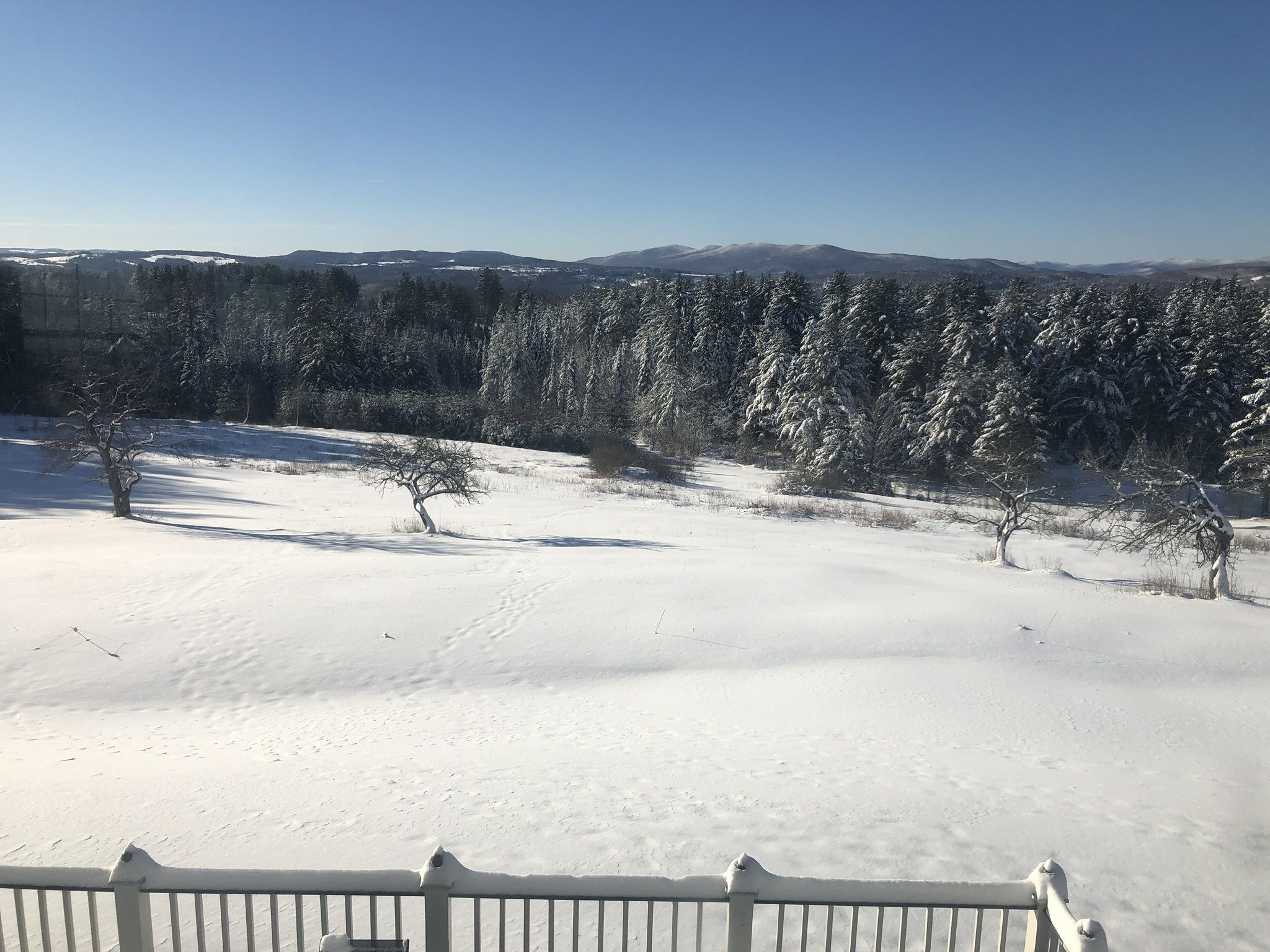 Een besneeuwd landschap met een heldere lucht, een omheind gebied en een bergketen in de verte.
