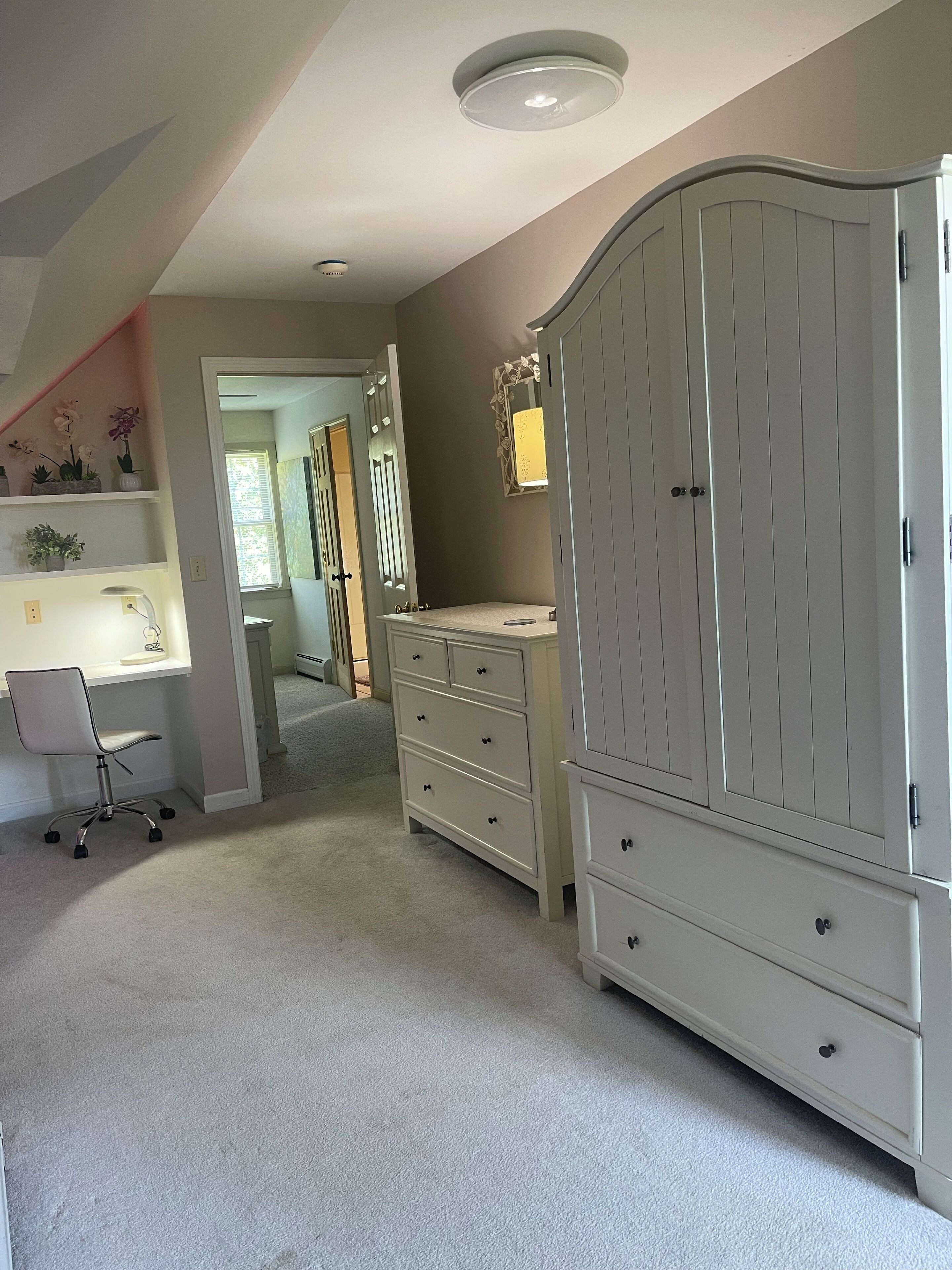 A bedroom with a desk, a large wardrobe, and a staircase leading to another room.