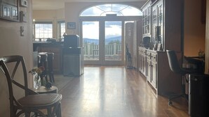A spacious kitchen with wooden flooring, a dining area with a chair and table, and a view through a large window. - High Hill Inn (East Montpelier)