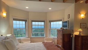 A bedroom with a large bed, two windows with a view, a dresser, and a lamp. - High Hill Inn (East Montpelier)