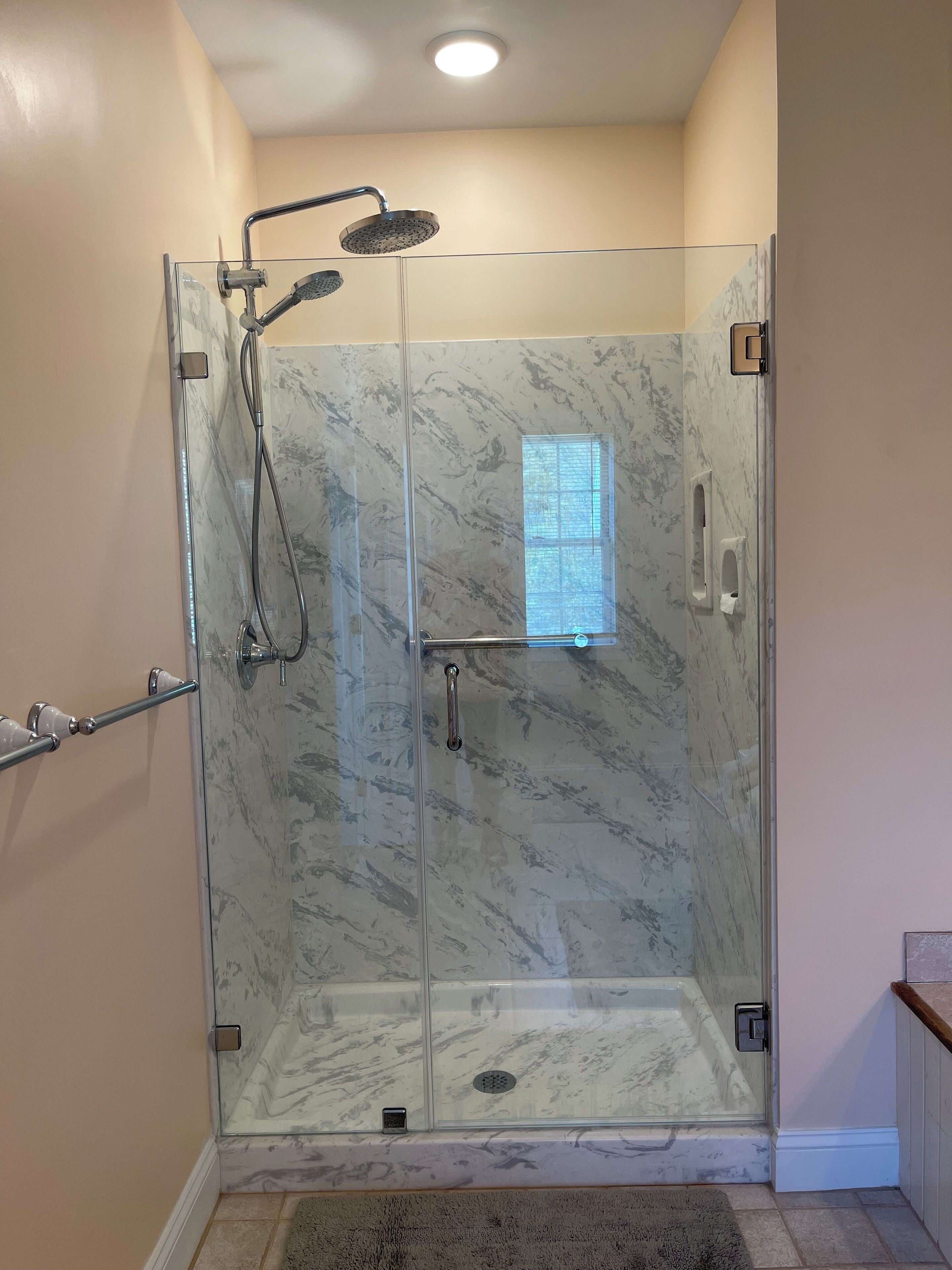 A glass-enclosed shower with a marble finish, a handheld showerhead, a handheld showerhead, a handheld showerhead, and a handheld showerhead.