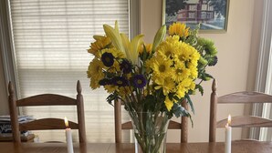 A dining table set with white plates, gold cutlery, and a vase of yellow flowers. - High Hill Inn (East Montpelier)