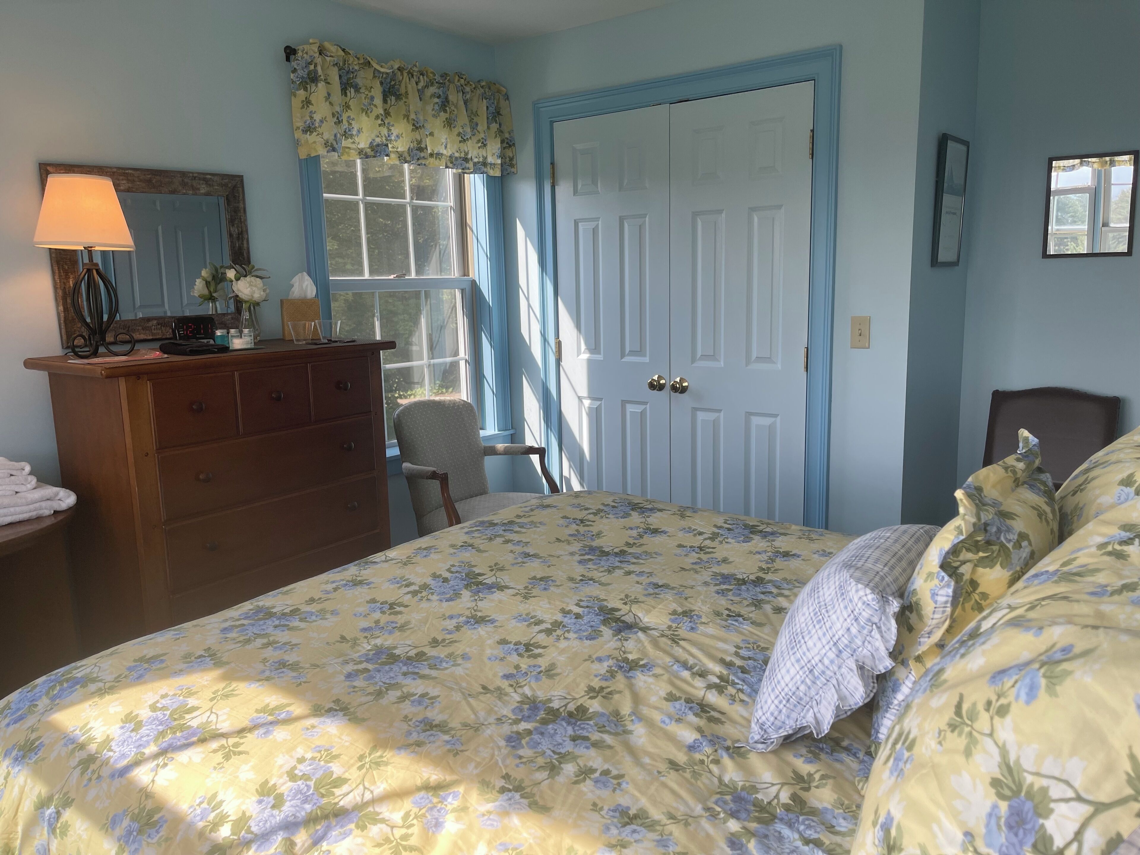 Une chambre à coucher avec un lit, une commode, une chaise et une fenêtre avec des rideaux.