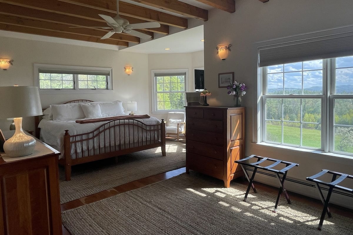 A bedroom with a bed, dresser, and a window with a view of greenery.