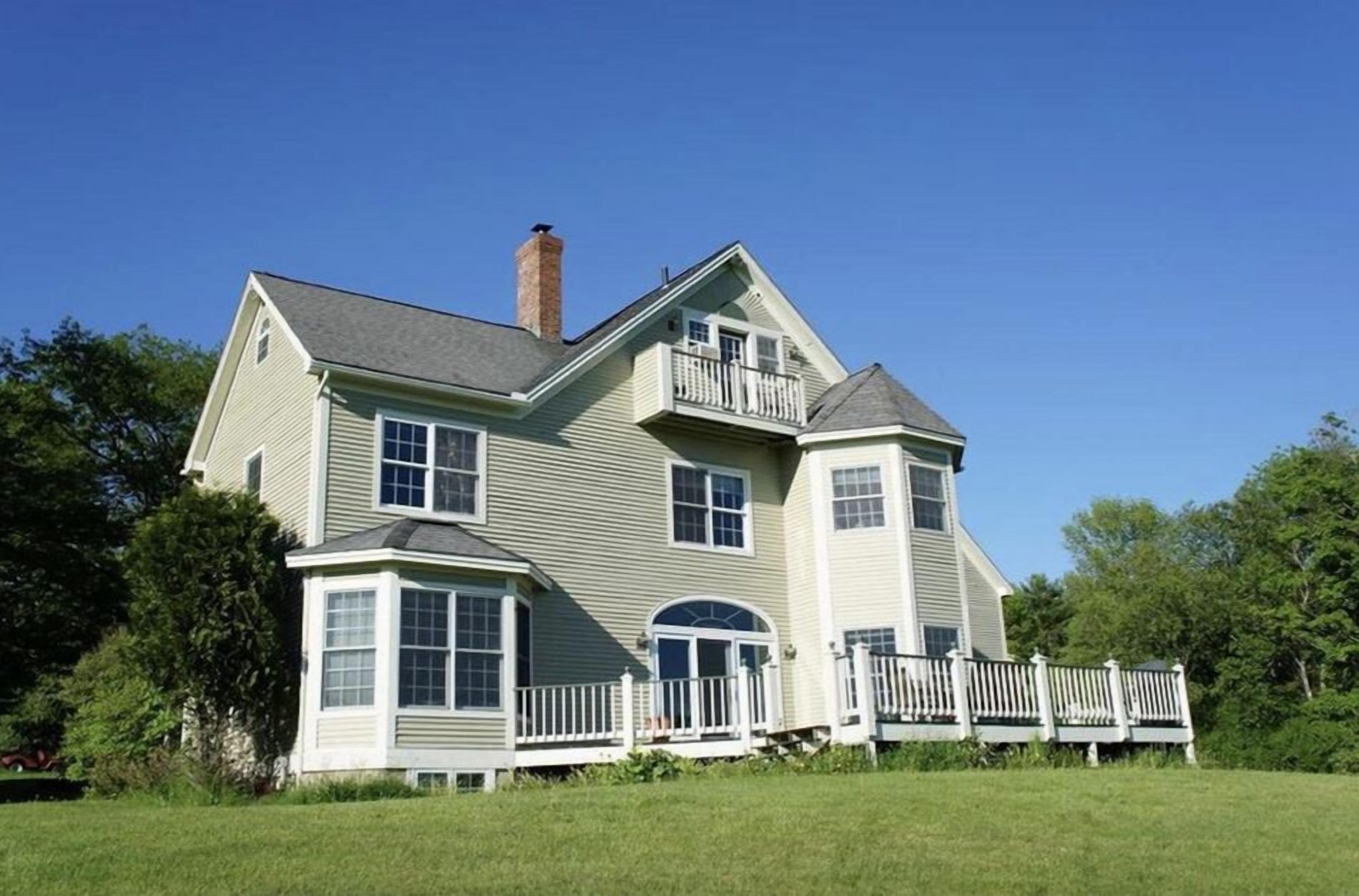 Une maison à deux étages avec une véranda qui fait le tour de la maison, une cheminée et un petit balcon.