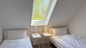 Une petite chambre avec un seul lit, une lucarne et une table de chevet avec une lampe.