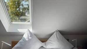 Une pièce avec une lucarne, des murs blancs et deux coussins blancs sur un lit en bois.