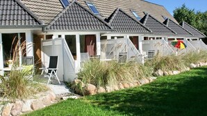 Une rangée de maisons avec des toits inclinés et des lucarnes, une pelouse verdoyante et un petit espace piscine.